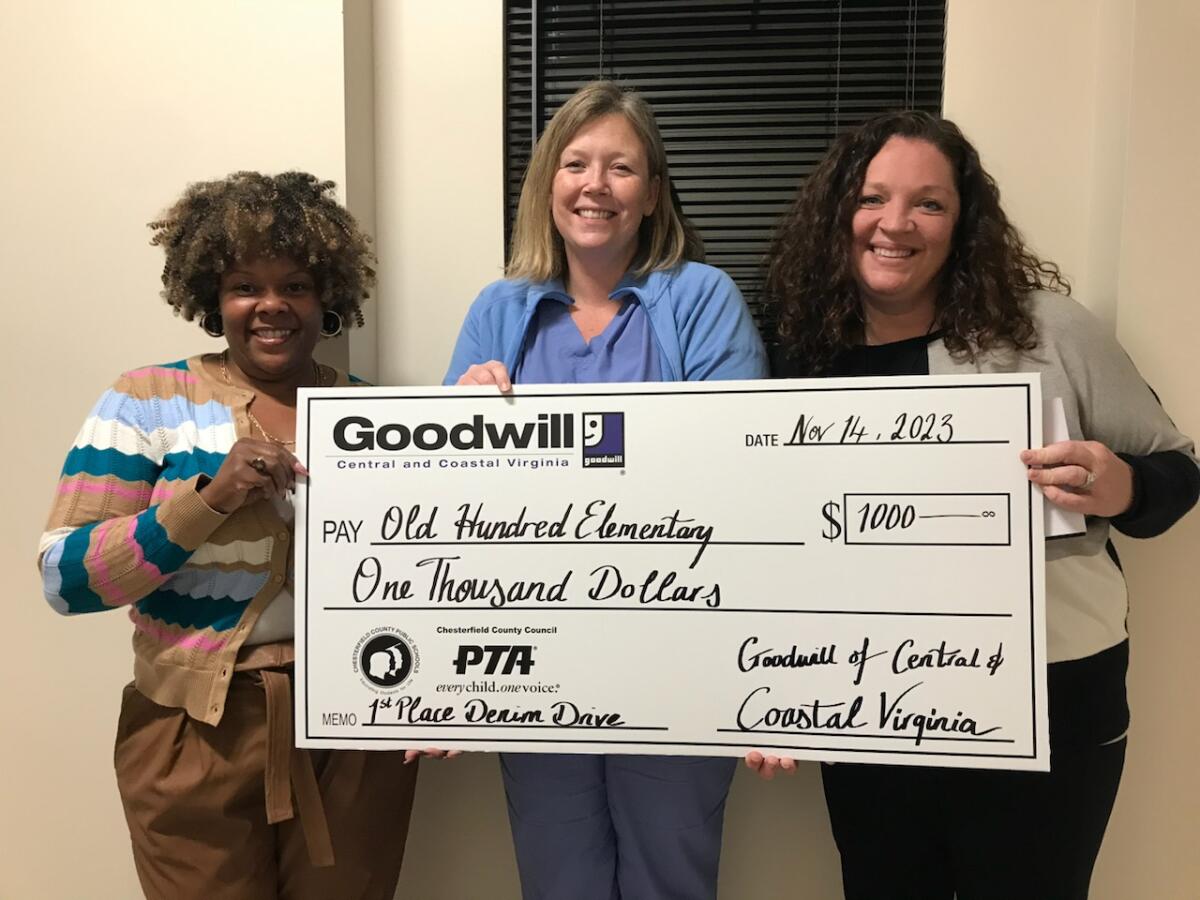 Three women stand side by side, holding a check from Goodwill of Central and Coastal Virginia to Old Hundred Elementary School for $1000. Alicia Broughton, Principal, Stephanie Watson, PTA Secretary, and Tammy W. McCain, Manager Donor Development for Goodwill, smile as they celebrate the generous donation for the school's Denim Drive.