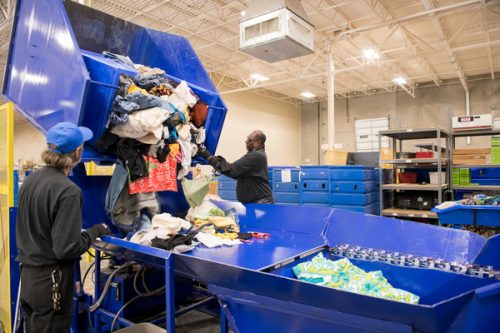 Goodwill employees operate machinery to process and sort textiles, highlighting Goodwill's salvage and broker expertise.