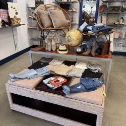Mini dorm room display at a Goodwill store featuring jeans, shoes, books, pillows, a chair, lamp, and decorative items like a globe and wall art.