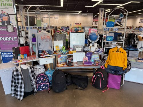 Back-to-school display at a Goodwill store featuring backpacks, school supplies, college gear, clothing, and dorm essentials like storage bins and décor items.