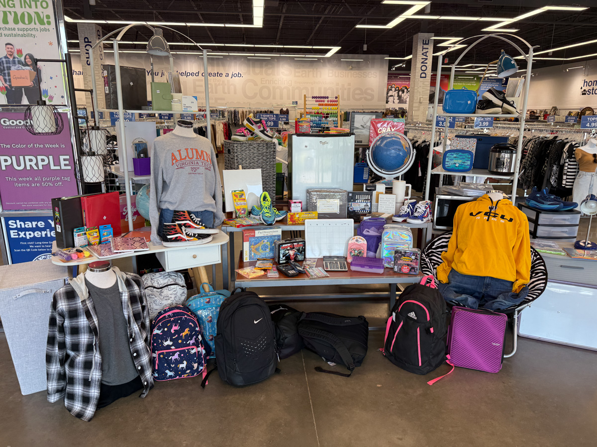 Back-to-school display at a Goodwill store featuring backpacks, school supplies, college gear, clothing, and dorm essentials like storage bins and décor items.